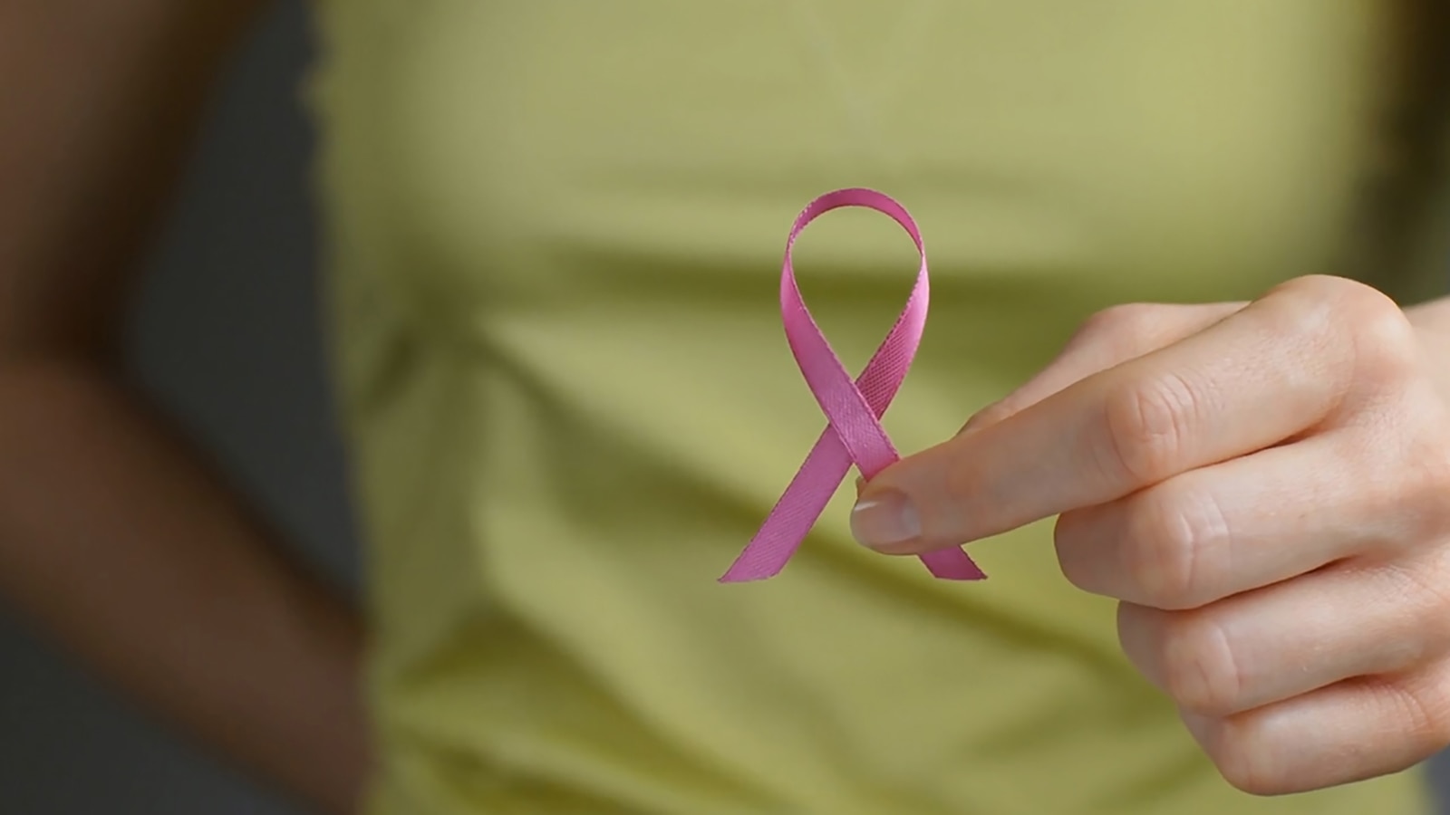 A woman holds up a pink breast cancer awareness ribbon.