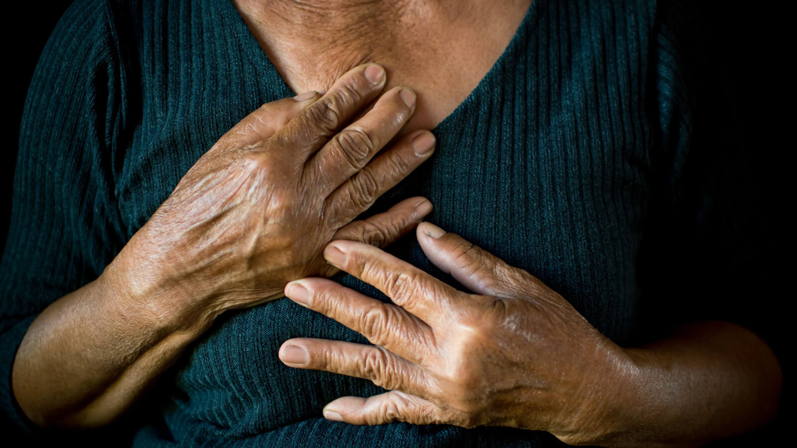 A close-up of an older woman holding her hands to her chest.