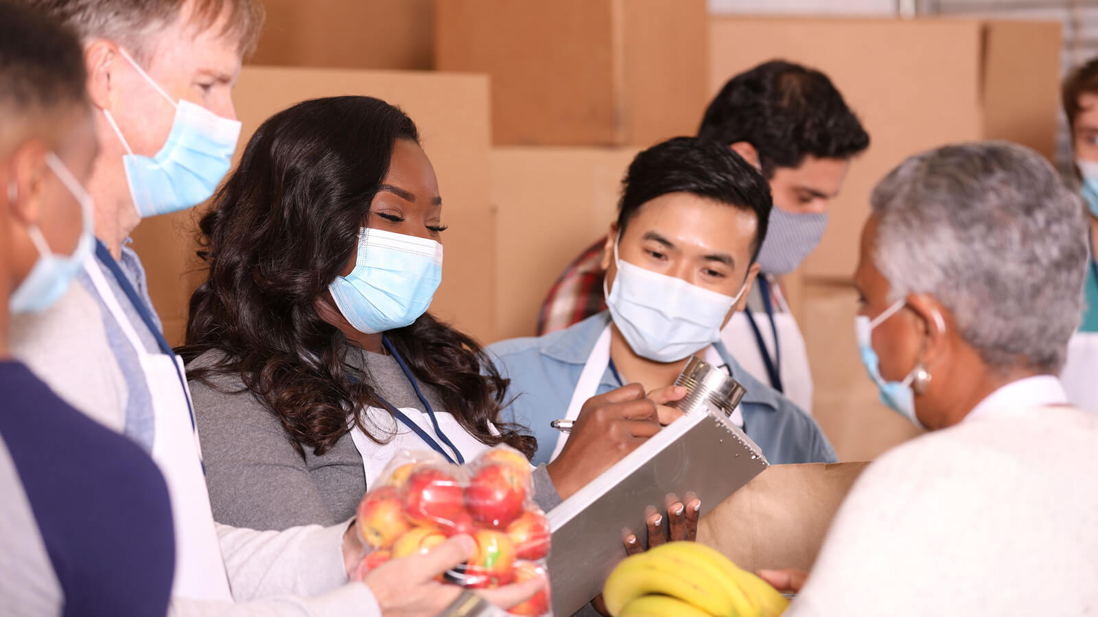 A group of masked volunteers tally food at a food bank.