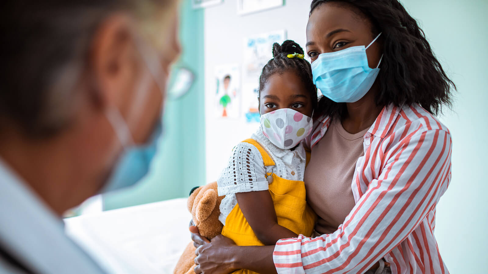 A mother holds her daughter as they speak to a healthcare provider.