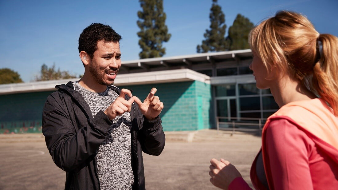 A young man using sign language to communicate in a conversation with a woman