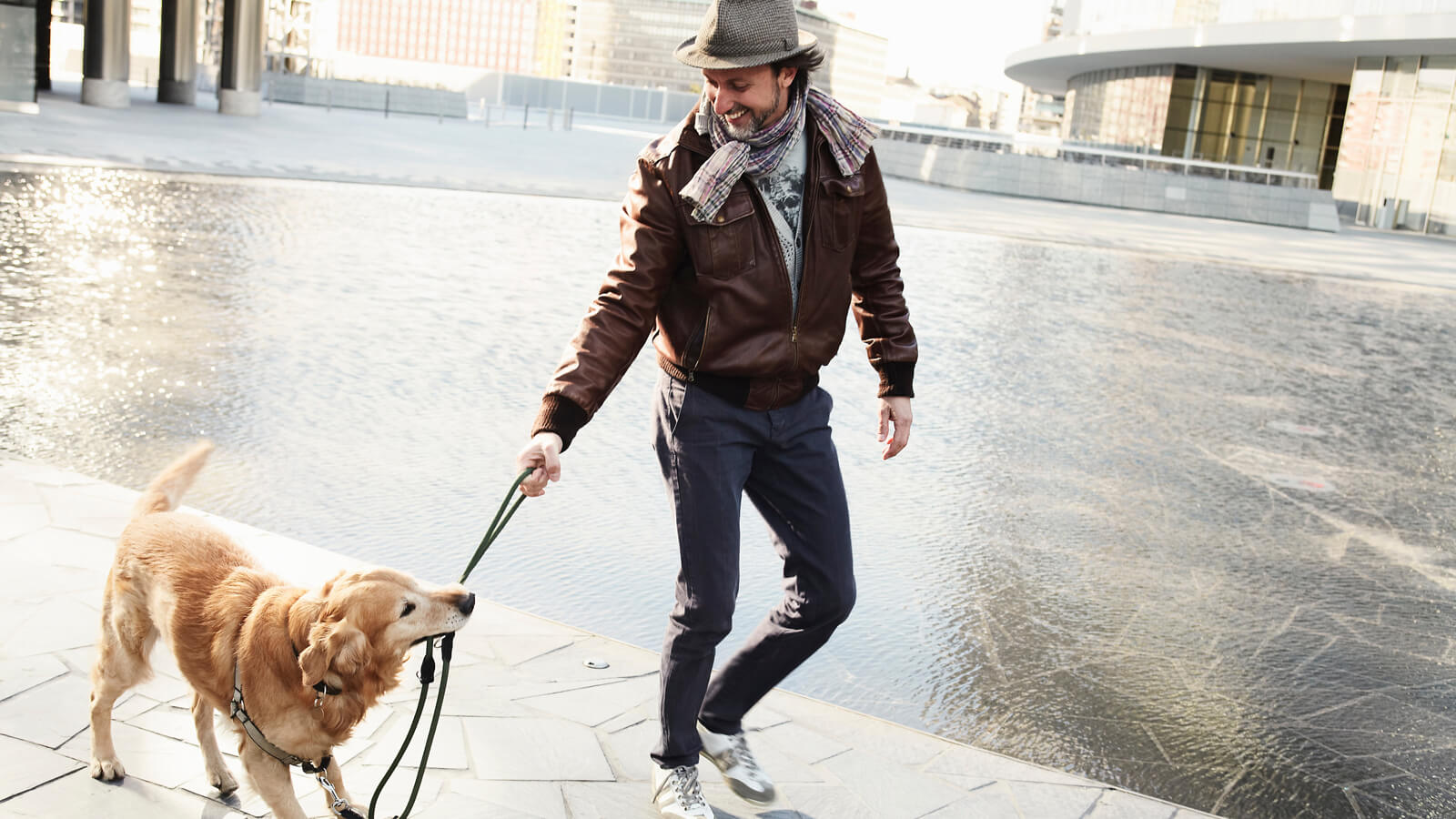 A man walks his dog who playfully tugs at its leash.