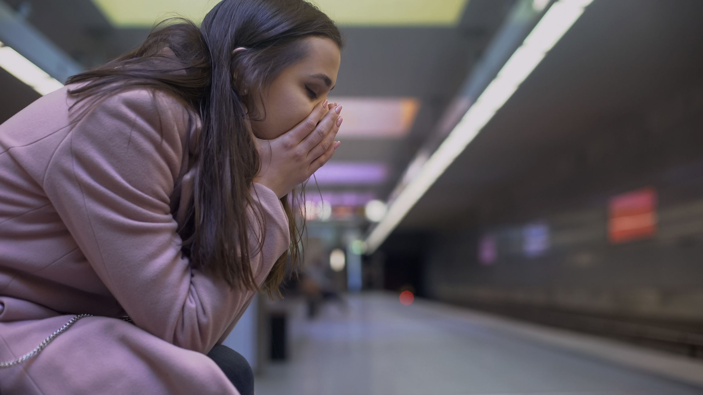 A woman sits with her hands over her mouth in a subway station.