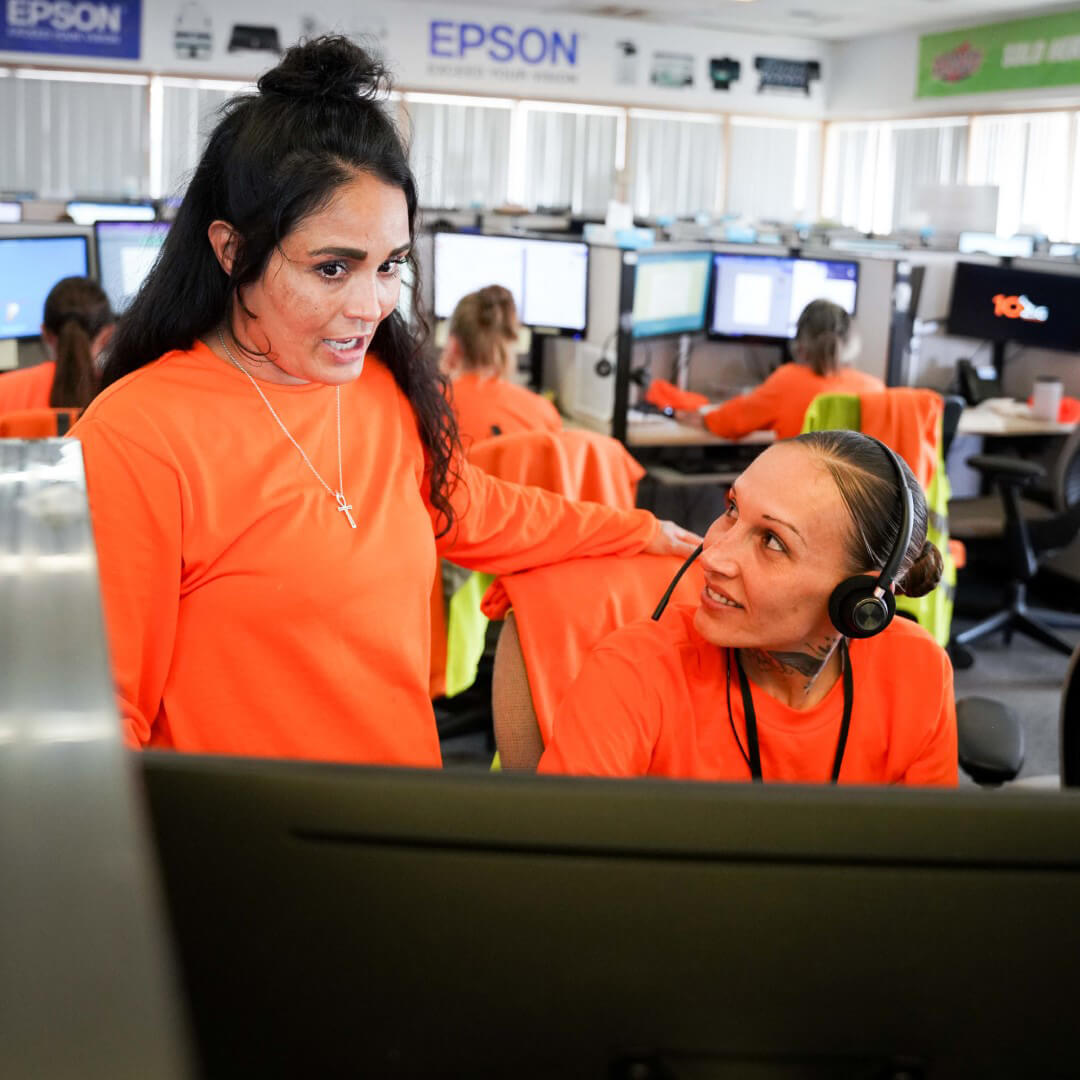 Two incarcerated women confer in a tele-office setting. Epson logos can be seen in the background.