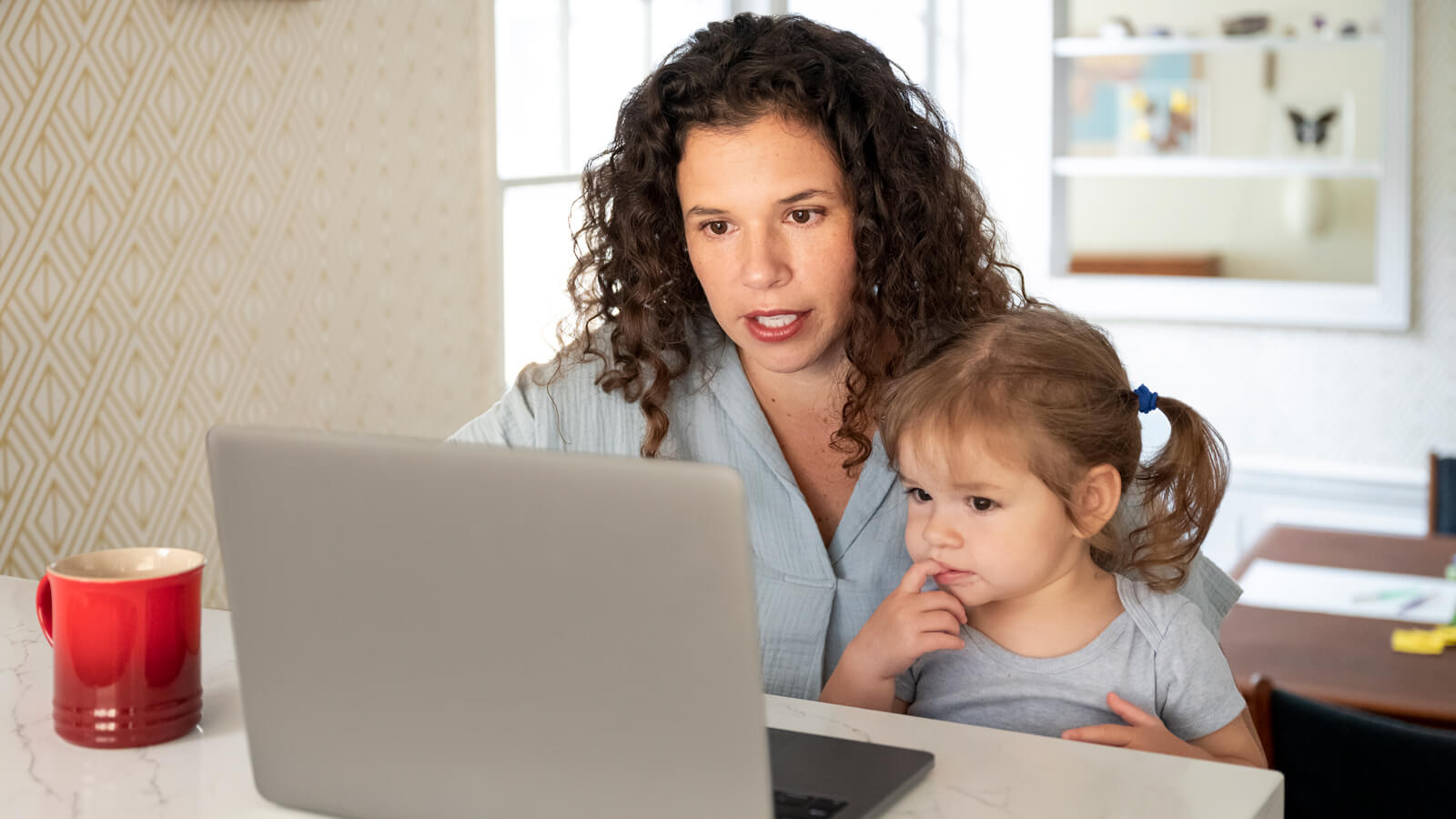 A mother and her toddler daughter use a laptop together.