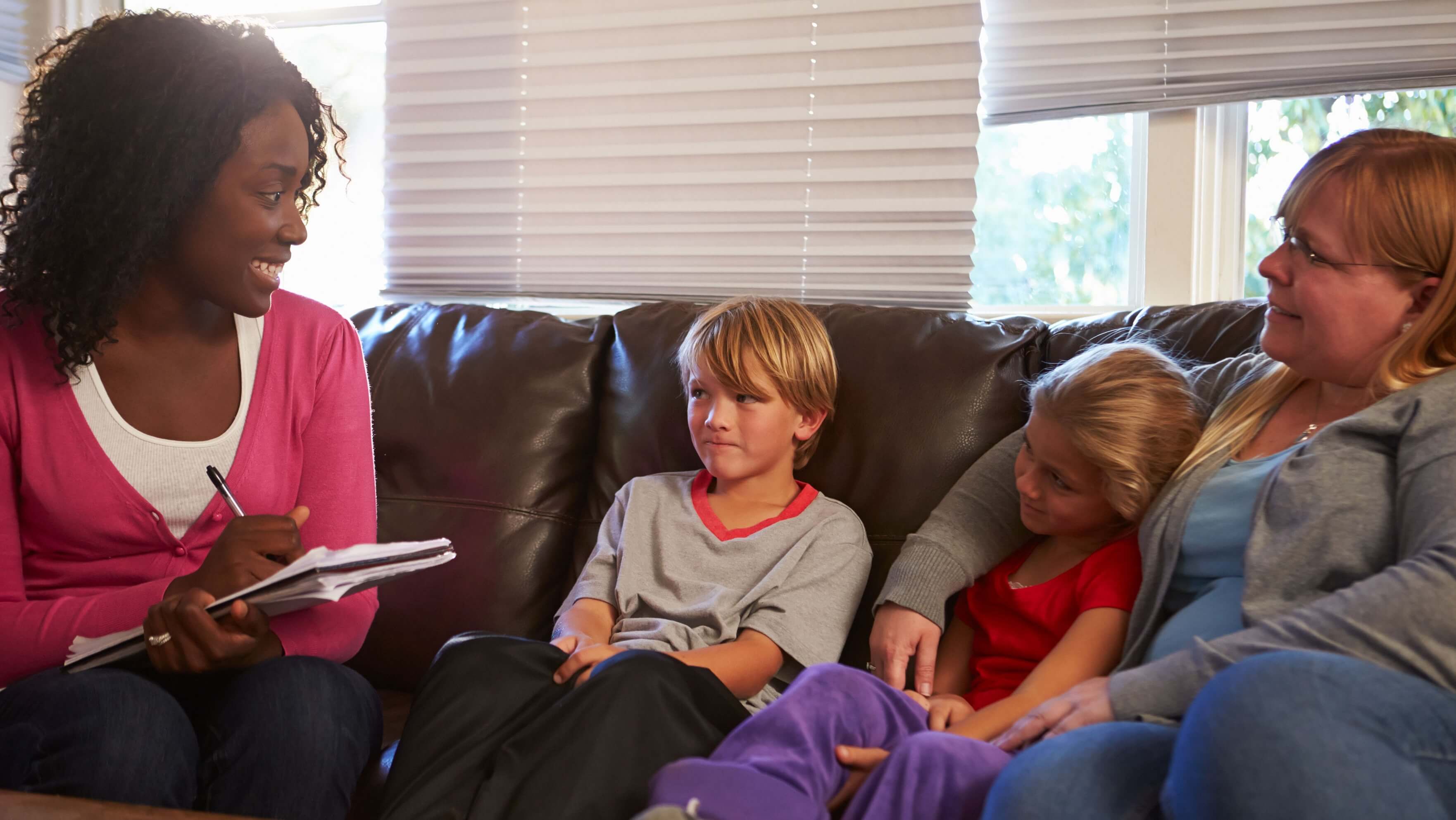A home visit with a clinician seated on a couch speaking to a mother and her two children