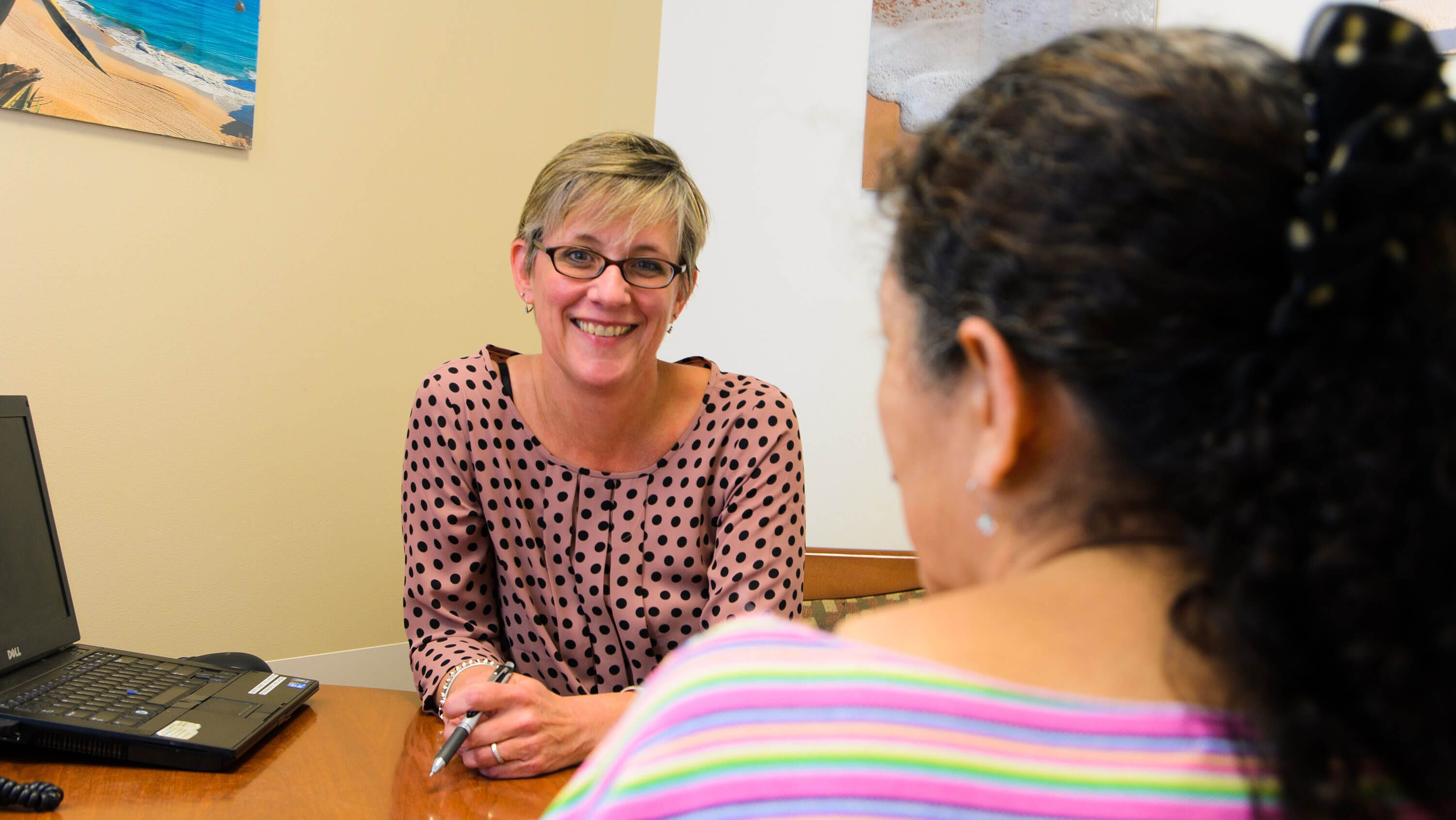A mental health counselor speaking to a client seated across the table from her.