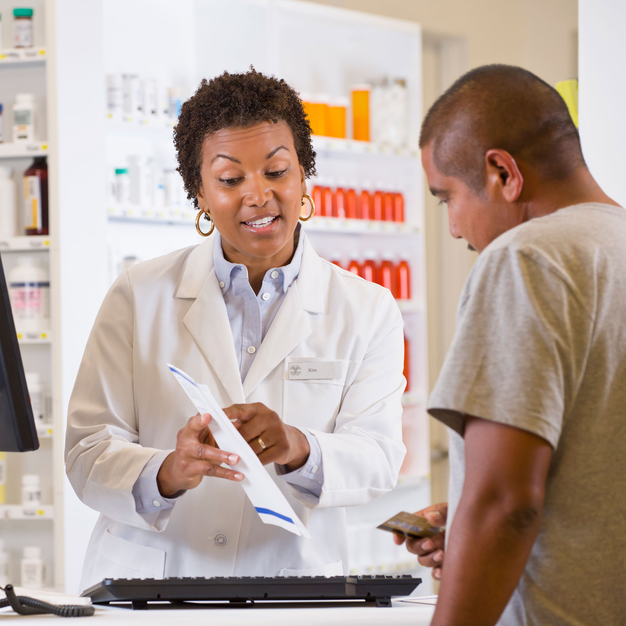 A pharmacist stands at the register and explains the prescription to a client.