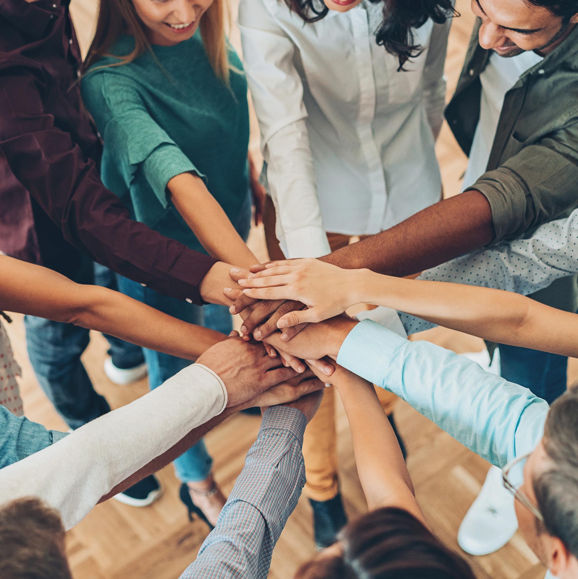 A circle of people extending their hands to the middle to create a hand pile.