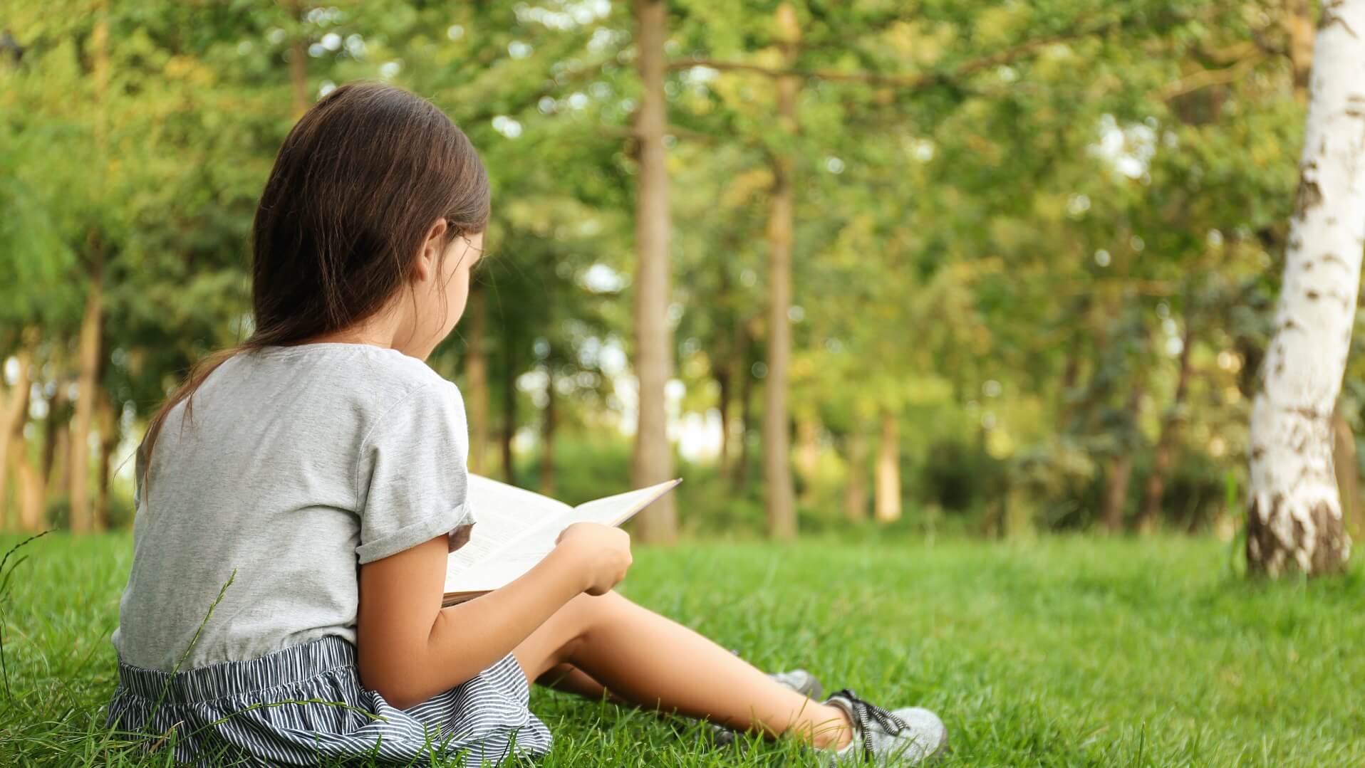 Young girl sitting in a grassy field reading a book