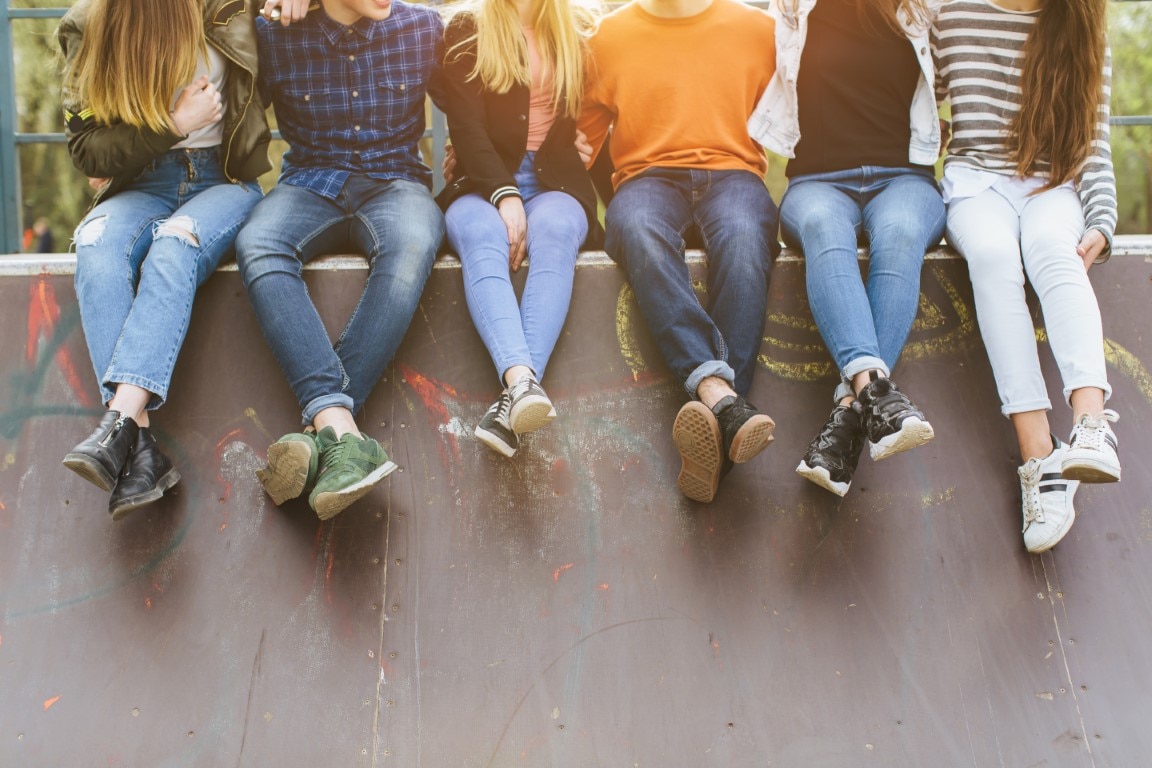 Six teenagers sit on a wall with their arms around each other