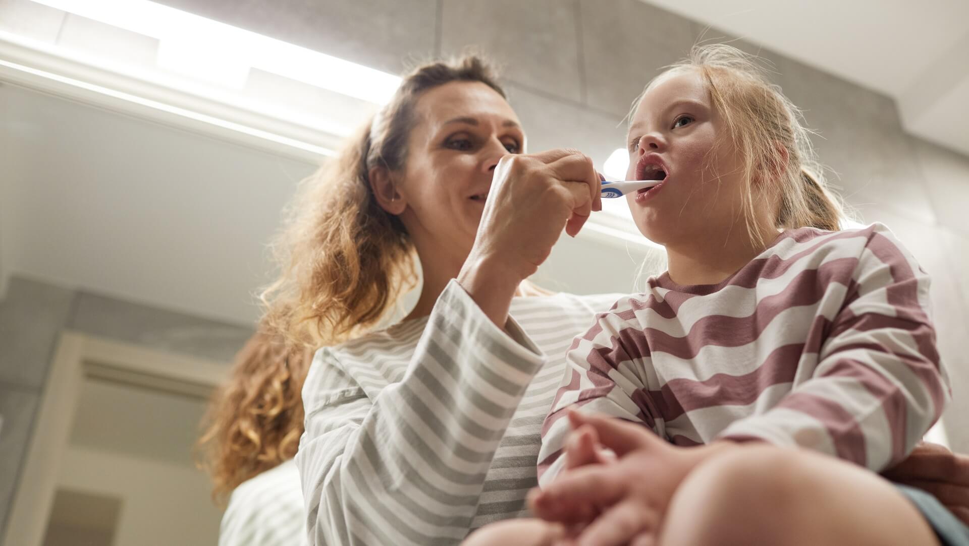 Caregiver assisting a child brushing their teeth