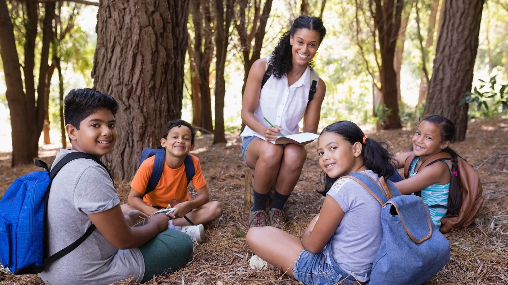 Four children in a circle in front of a teacher outdoors