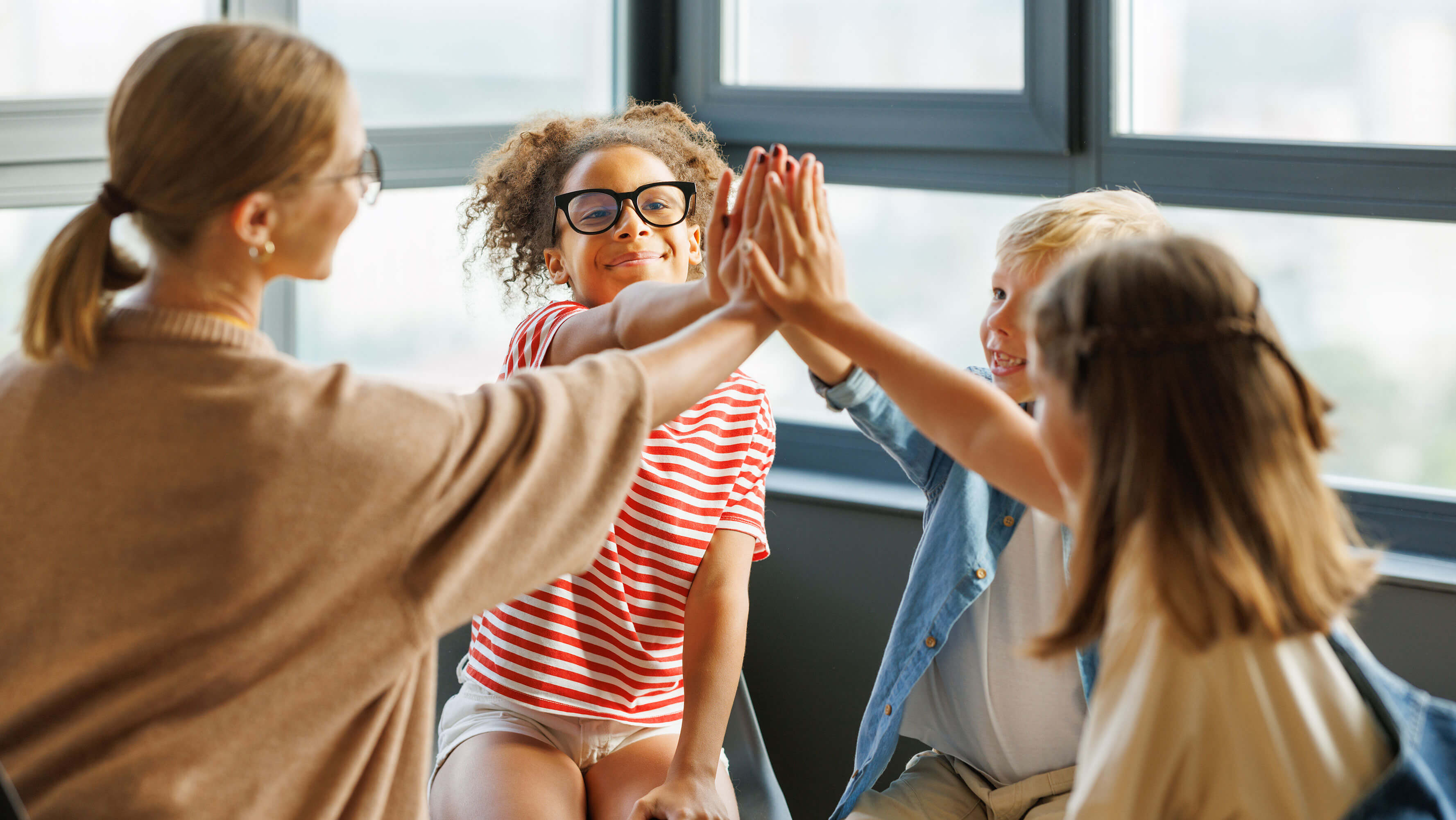 A small group of children with a teacher in a celebratory circle with their hands all together