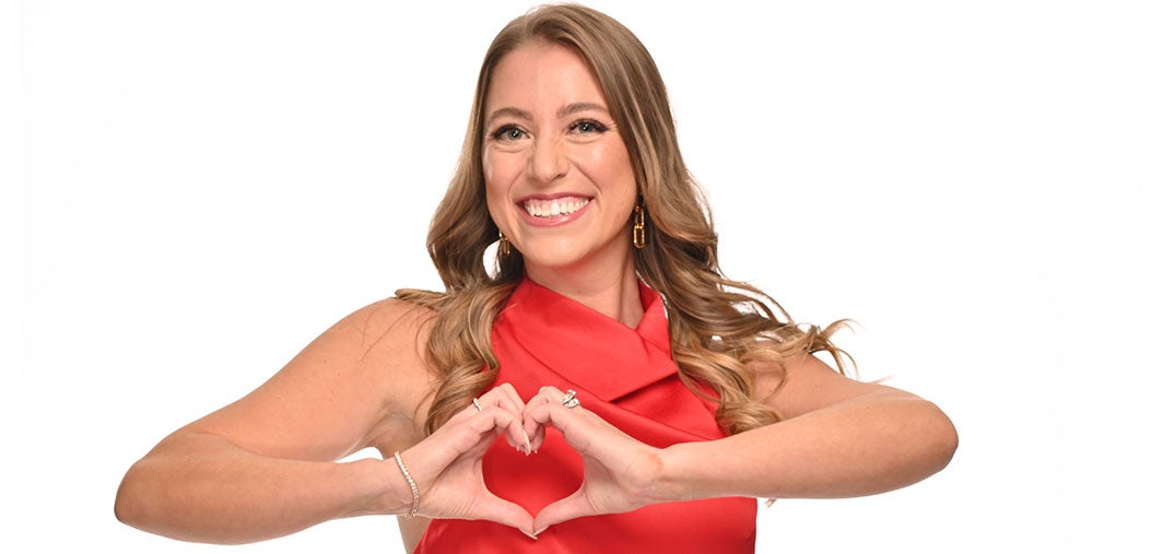 A woman in a red dress, flexing her muscles in a confident pose 