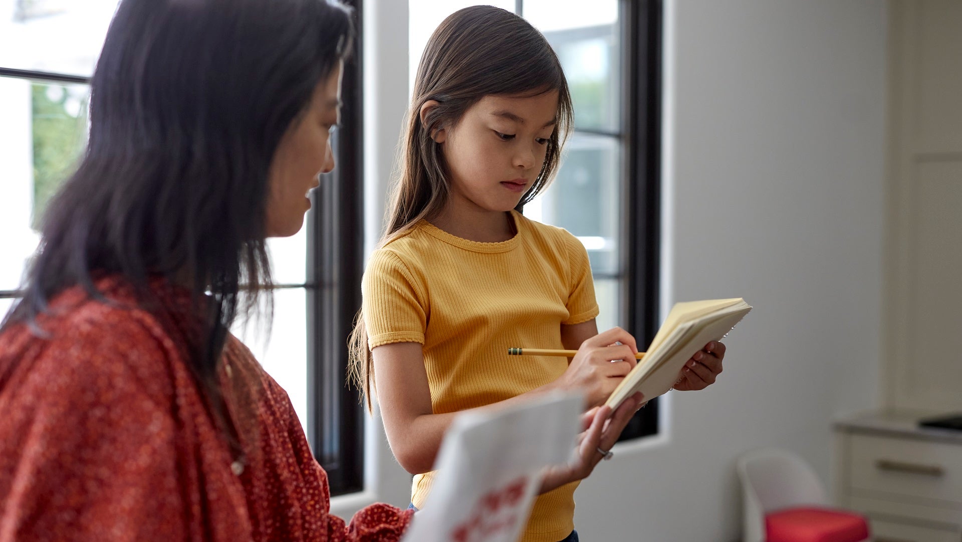 A woman and young girl look together and read from a notebook.