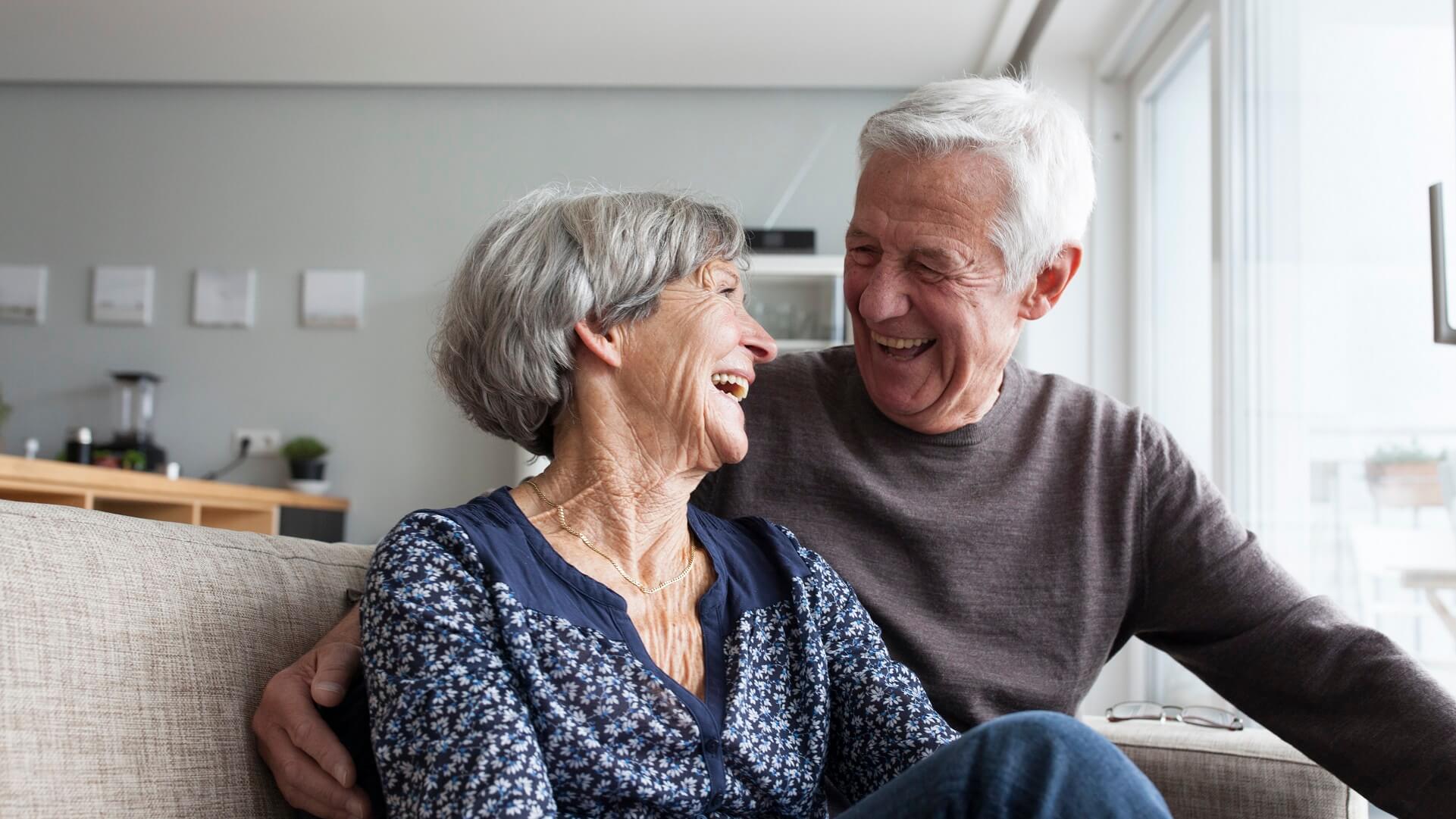 A man and woman laugh with each other at home. 