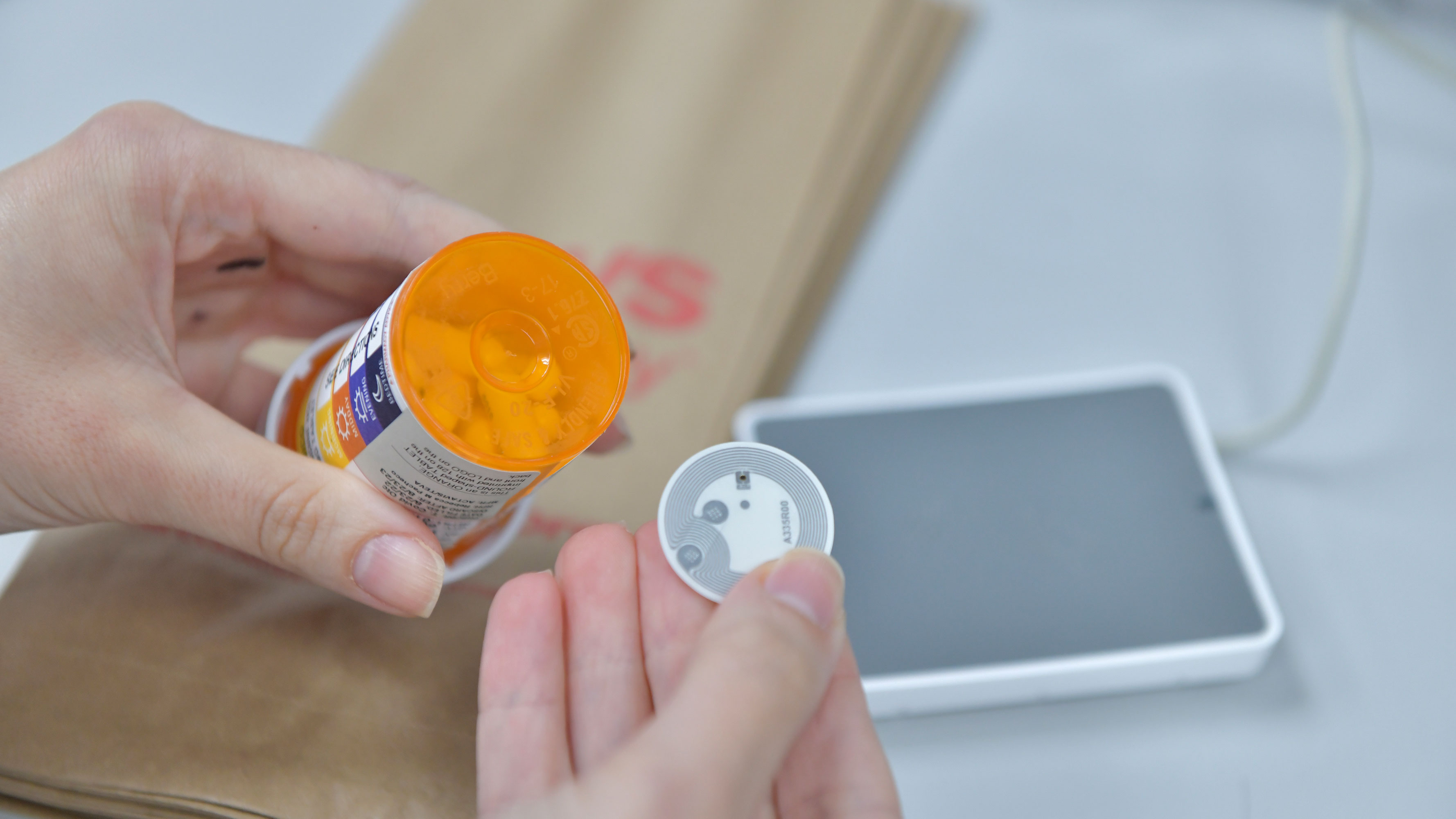 Person holding pill bottle equipped with RFID technology to read prescription label information aloud.
