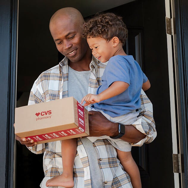 Father holding child while grabbing a CVS package from his porch