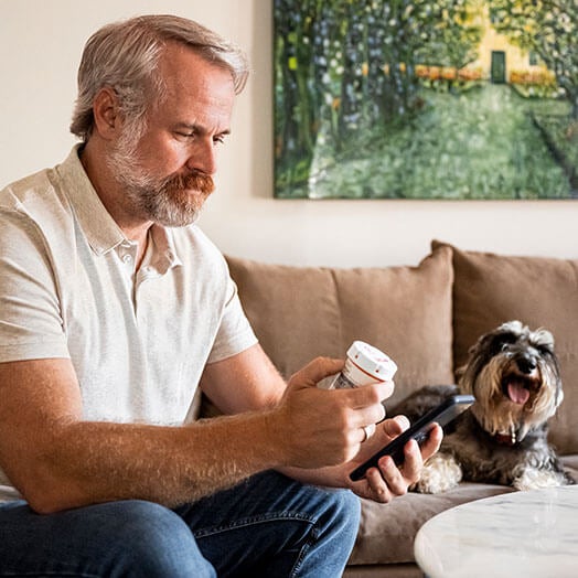 Male ording prescription refill at home on couch with dog
