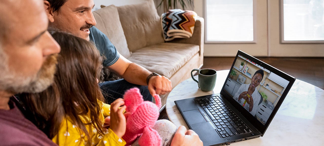 Two men and daughter at home on couch having virtual care appointment