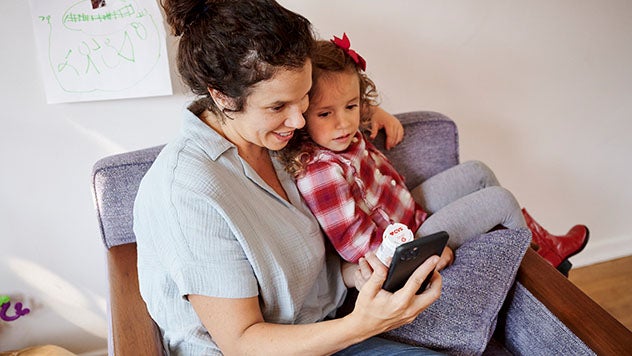 Mother holding daughter while refilling CVS prescription on mobile phone