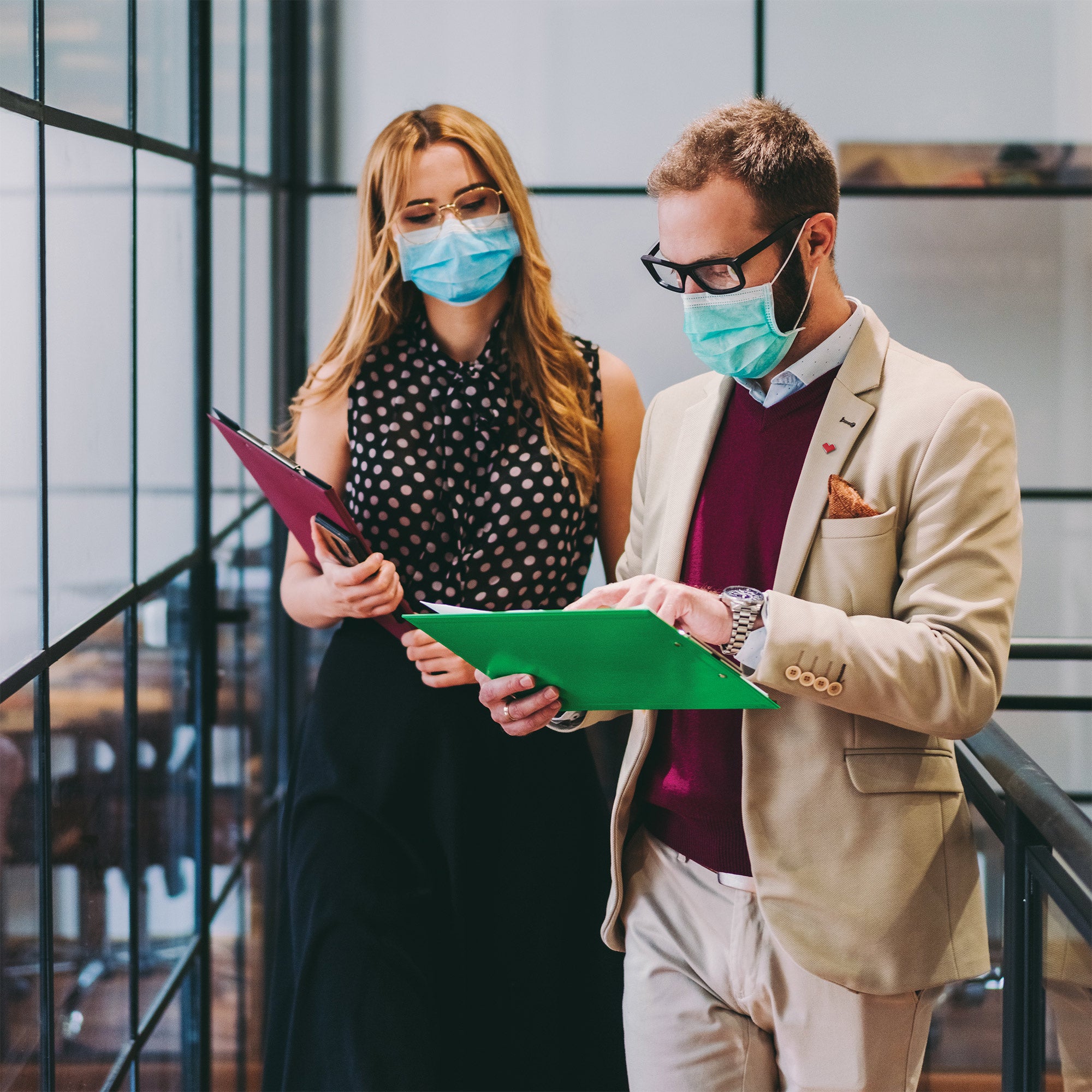 Two masked coworkers stand to have a quick meeting.