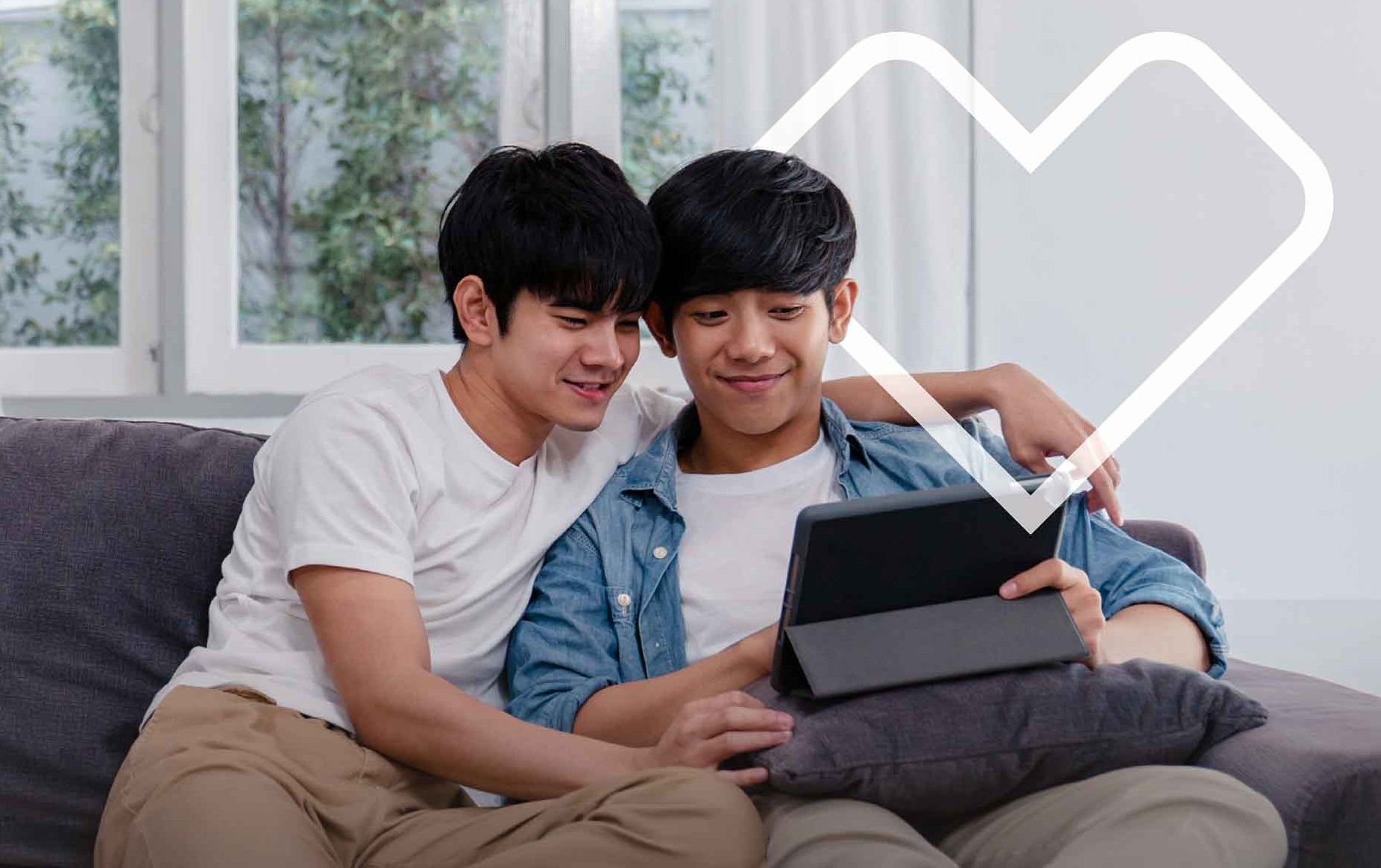 Two males sit on a sofa while browsing a tablet computer. The CVS Health heart outline is shown around them.
