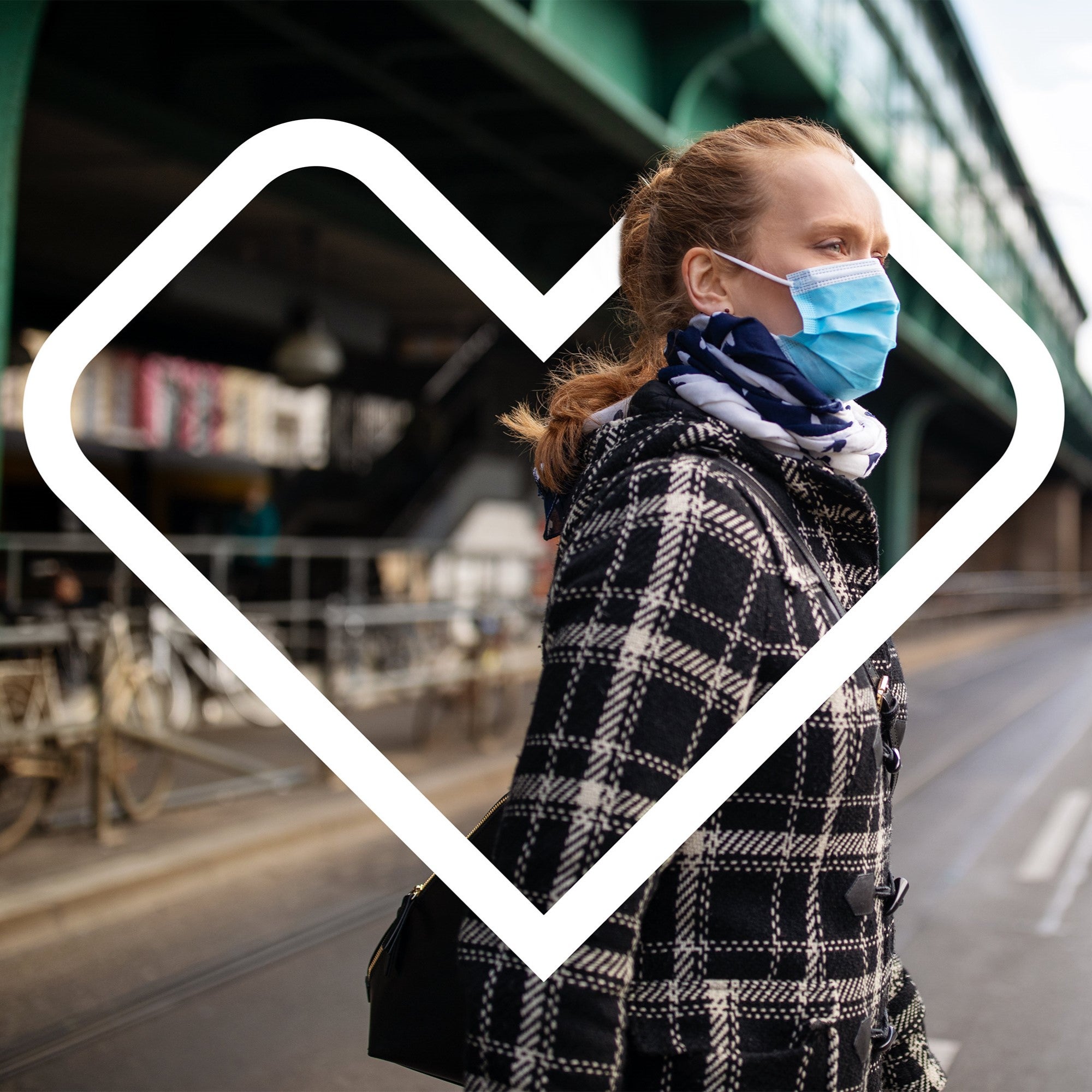 A woman, wearing a face mask, walks across a city street during her commute.