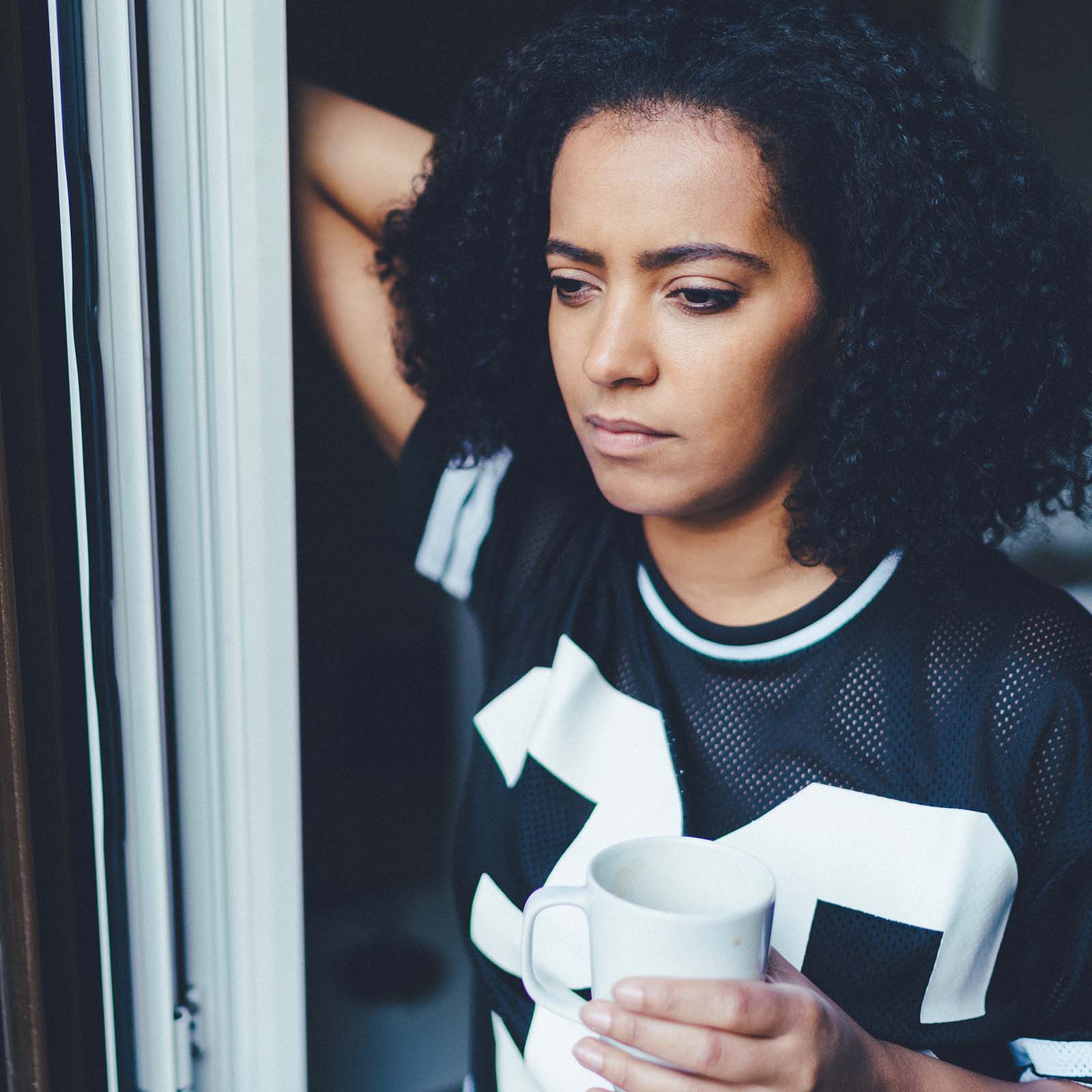 A woman looks out a sliding glass door while holding a cup of coffee.