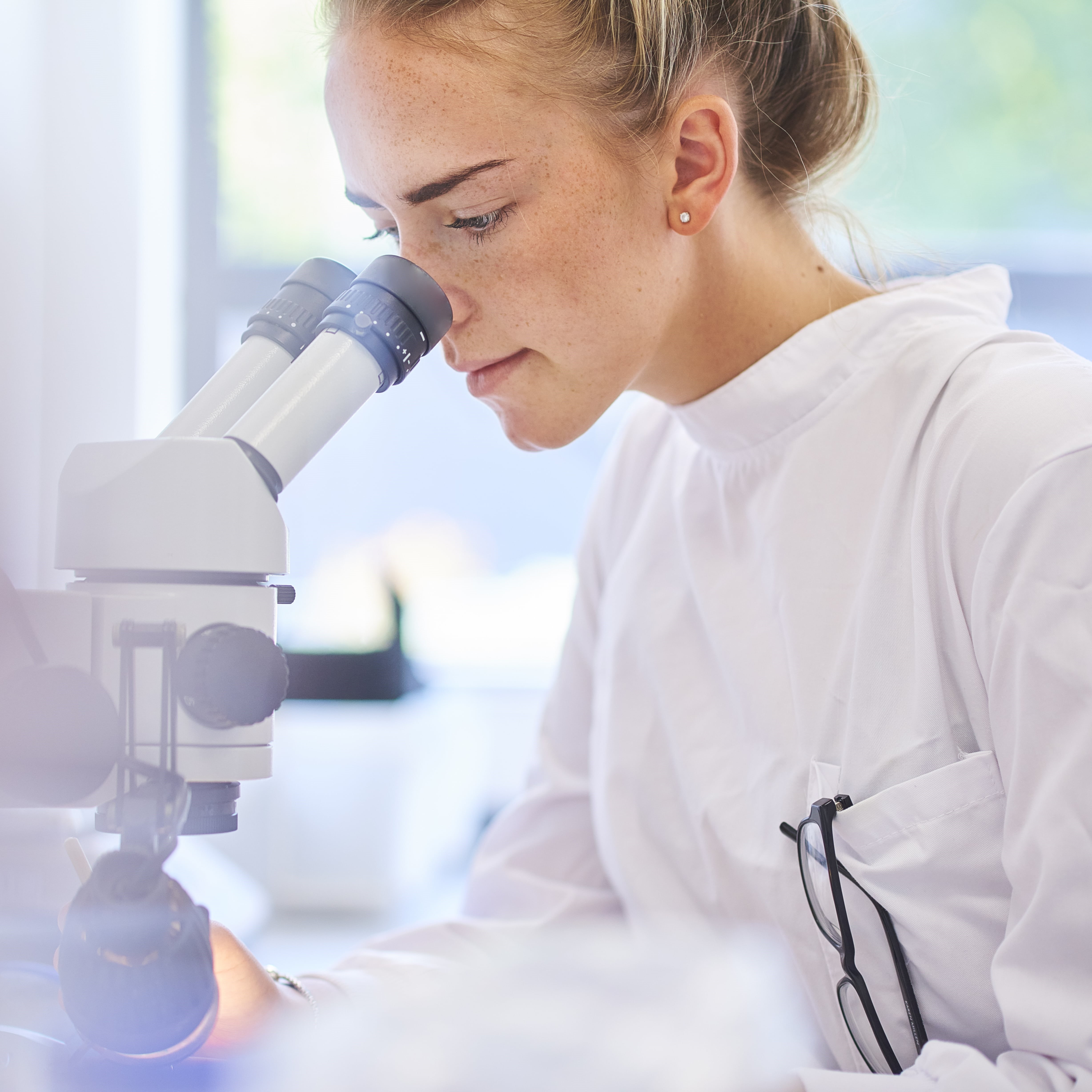 A lab technician looking through a microscope