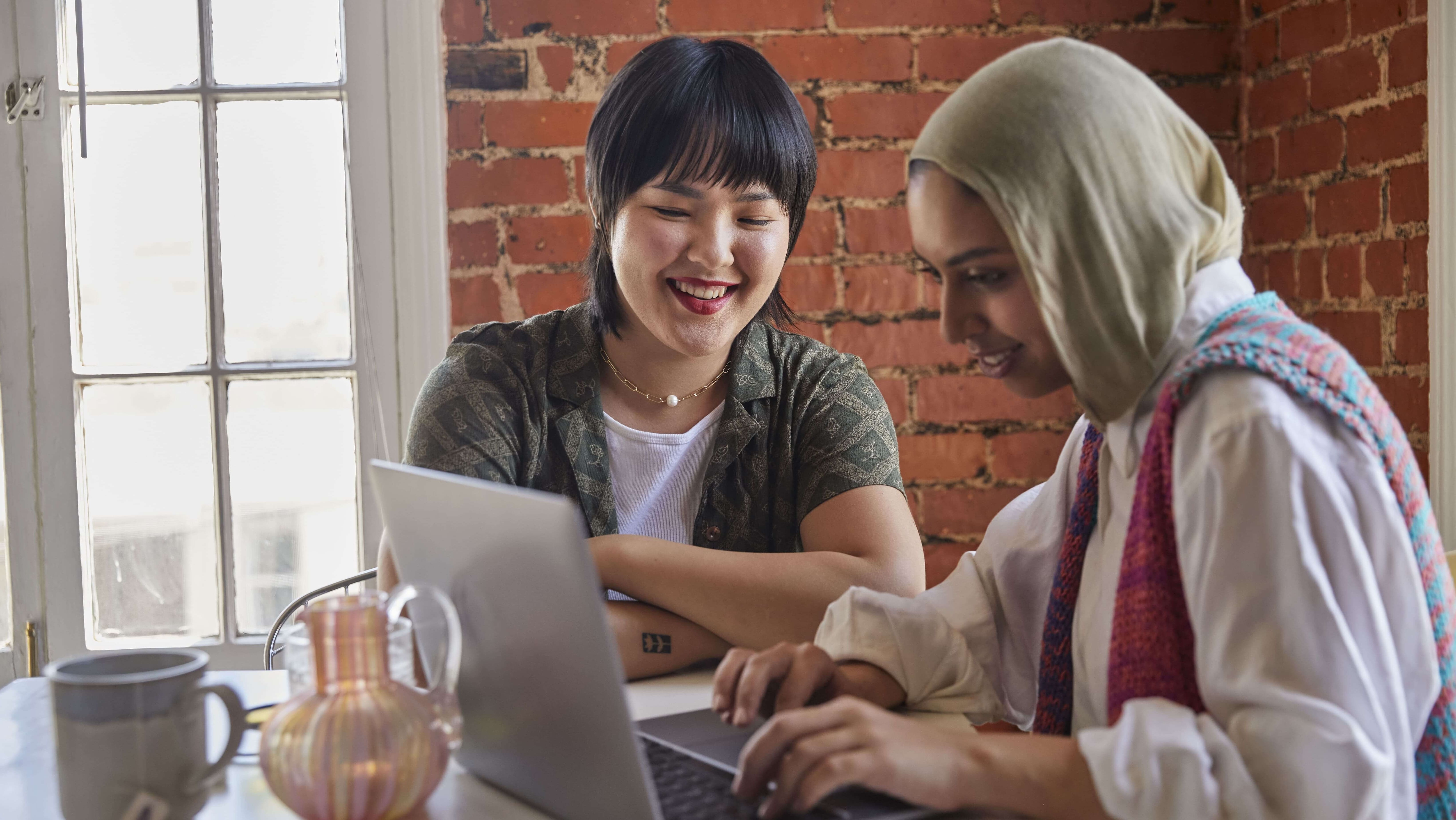 two women of color share a moment looking at a laptop.